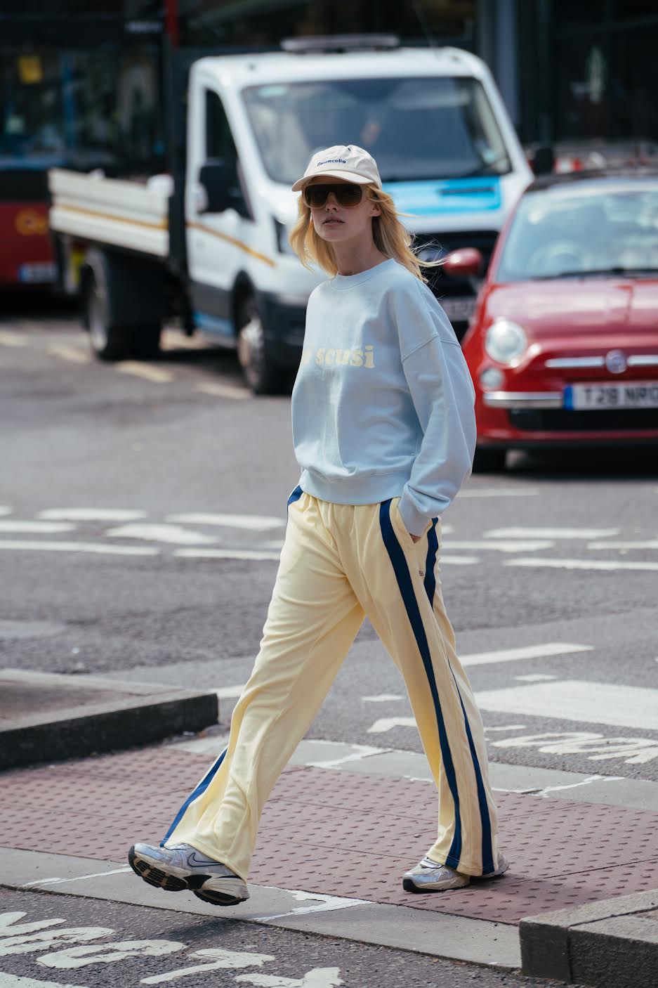 Person walking on a street wearing a light blue sweatshirt and yellow pants with a stripe.